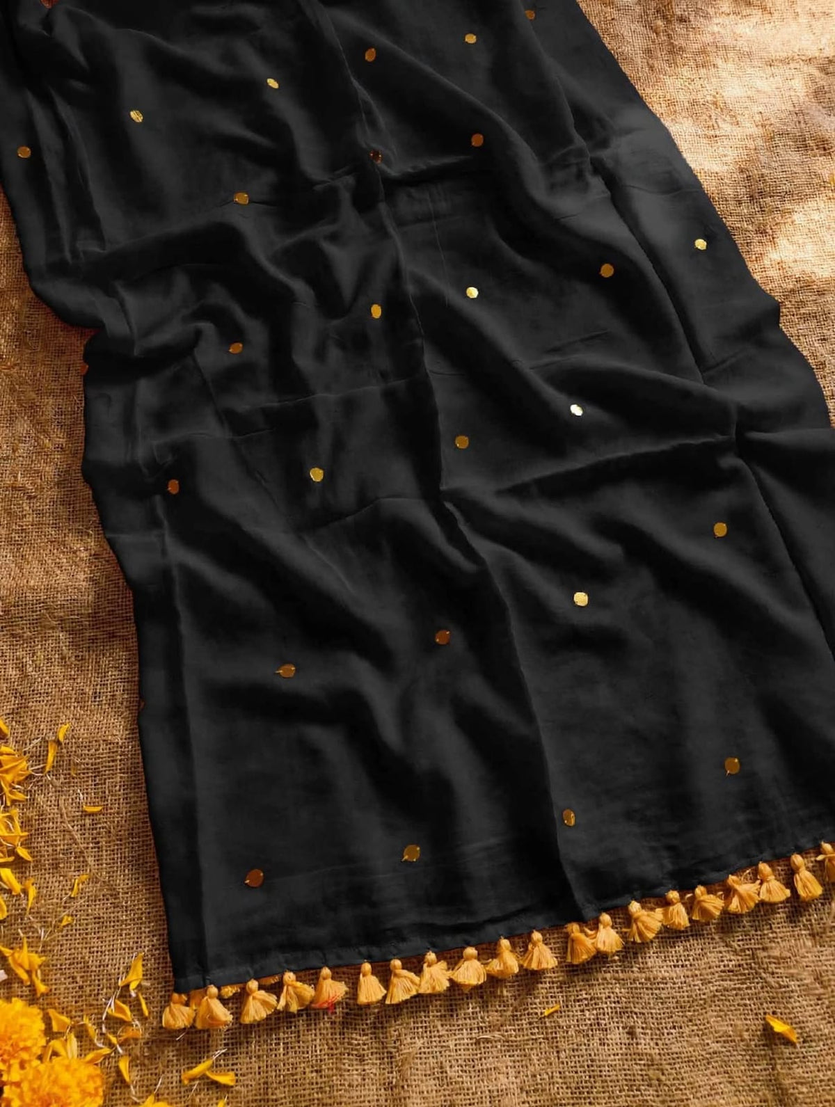 Black saree with scattered gold-toned sequins and golden-yellow tassels on a textured background