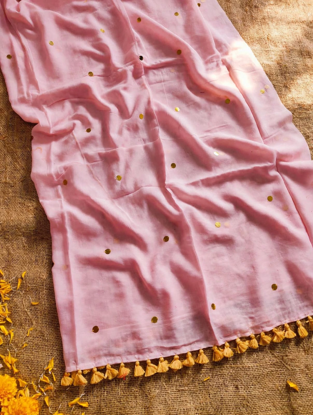 Soft pink saree with scattered gold-toned sequins and golden-yellow tassels on a textured background