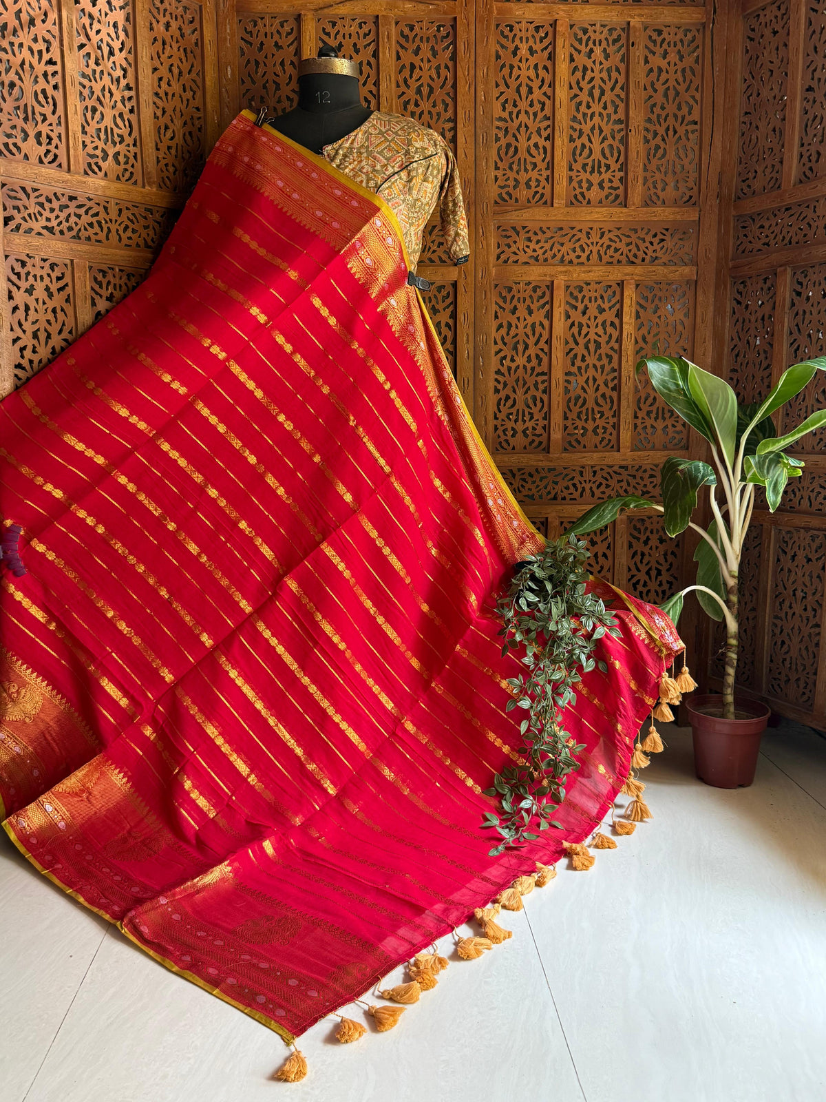 Red Ruhani saree displayed on a mannequin with gold-toned detailing, an ornate contrast border and tassels
